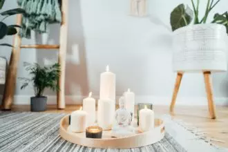 Wooden tray with burning candles and white Buddha statuette on the floor of modern interior.